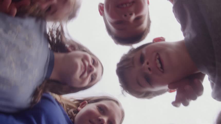 Five children gathered in a circle looking downward with bright sky in the background