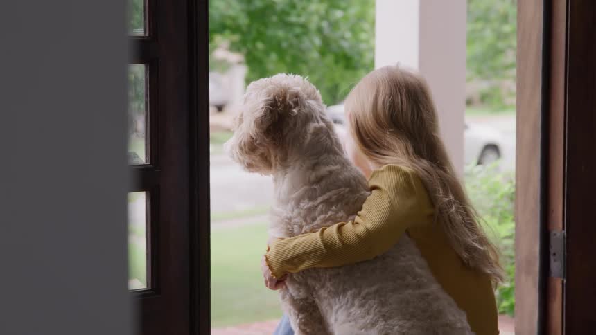 A girl child sitting with her pet dog at her home entrance in a suburb during daytime