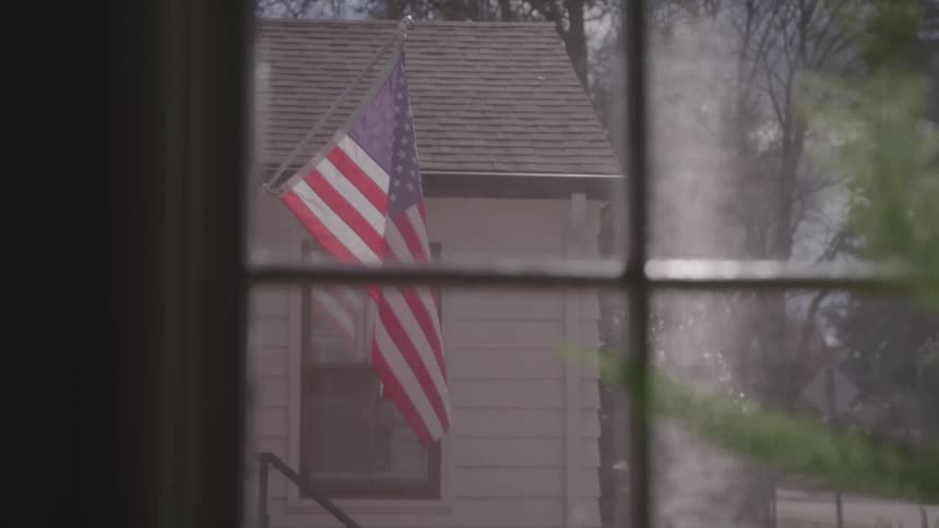 View through a window of an american flag flying outside of the house