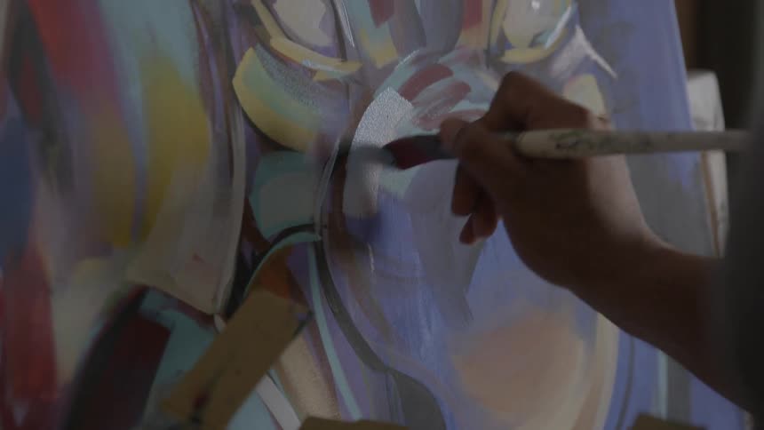 A person holding a cardboard with pain and painting on an easel