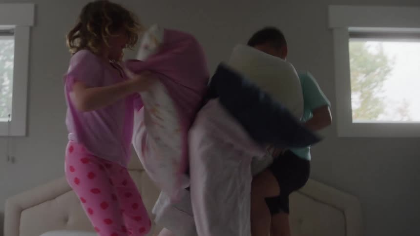 3 kids pillow fighting on a bed in a bedroom during daytime
