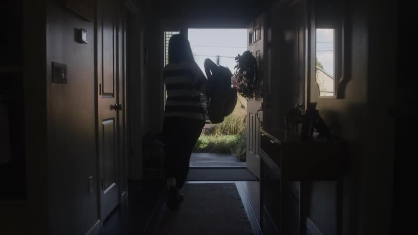 A female teenager picks up her backpack and walks away from home during daytime