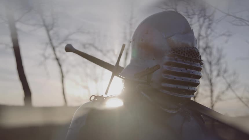 Person wearing medieval armor with sword on back in outdoor setting with dramatic light
