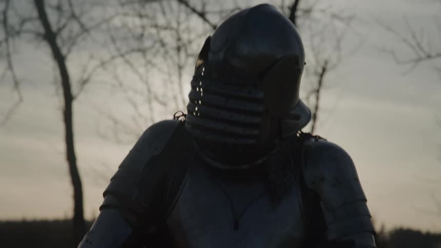 A person wearing medieval armor fighting with a sword against another person who is in front of them