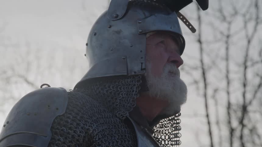 Close up portrait of an elderly man dressed as a medieval knight standing outdoors during daytime