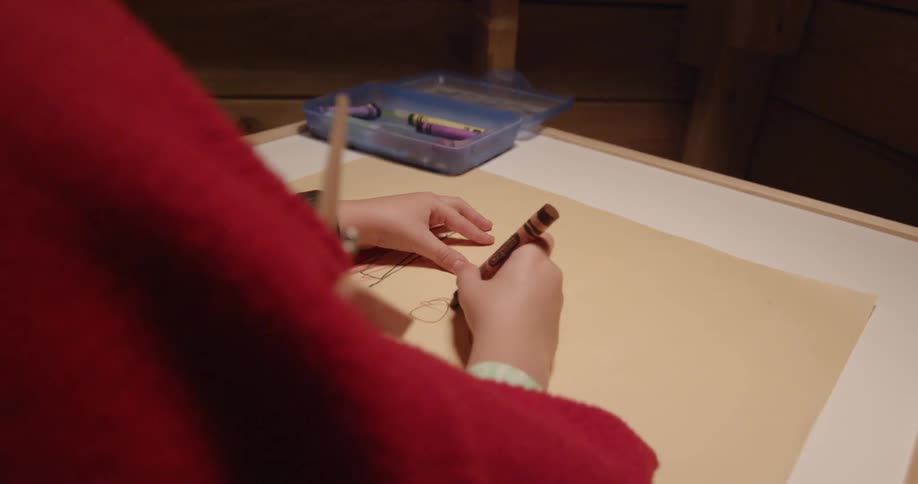Child sitting at desk drawing a picture with crayons