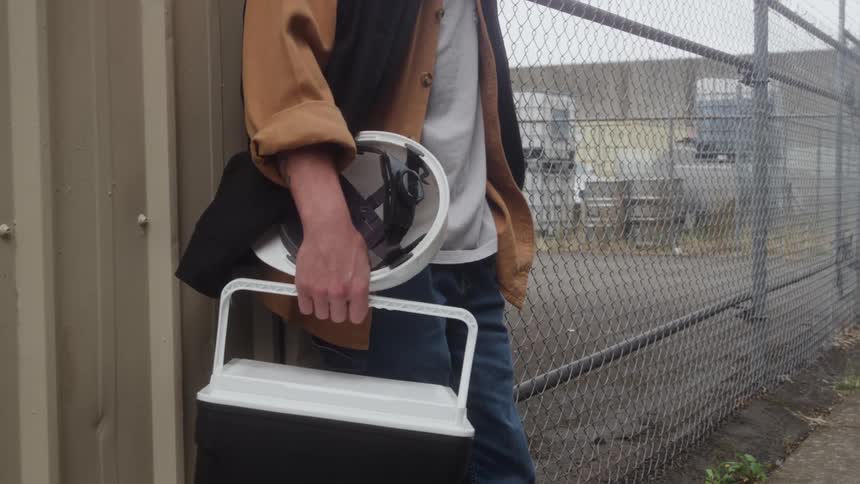 Person holds a cooler and circular object in an industrial area