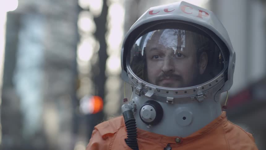 A man wearing a space helmet is standing in a city