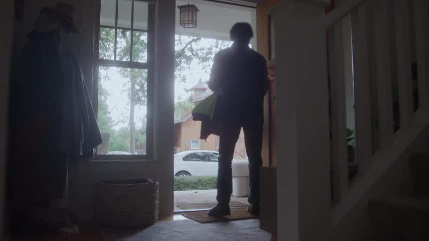 Man grabbing his vest and work tools and leaving through the front door of his house