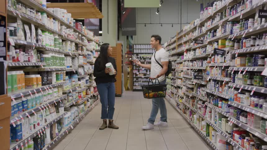 Two people exchanging a greeting in store aisle surrounded by supplement shelves