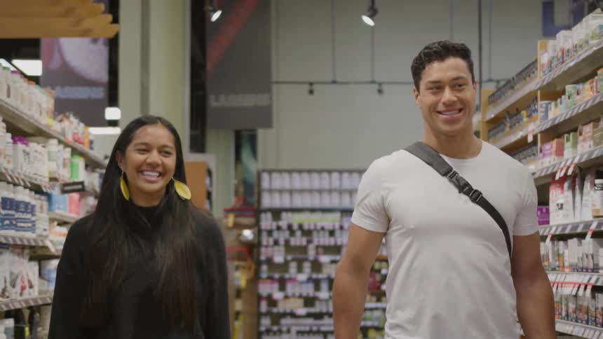 Two people walking through supplement and vitamin aisle chatting between welllit shelves