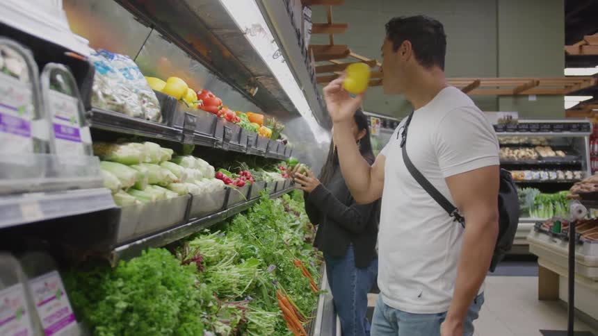 A man is shopping and picks up a yellow pepper