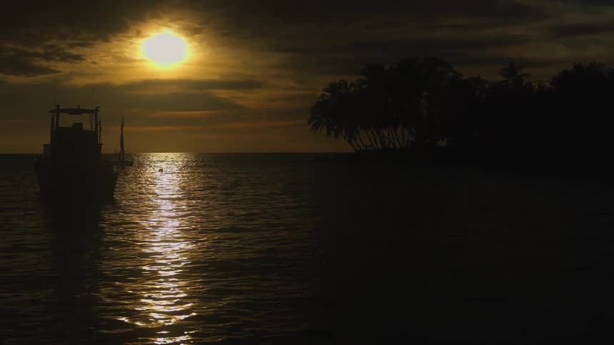 Peaceful sunset over ocean with golden reflection on water and silhouettes of boat and palm trees