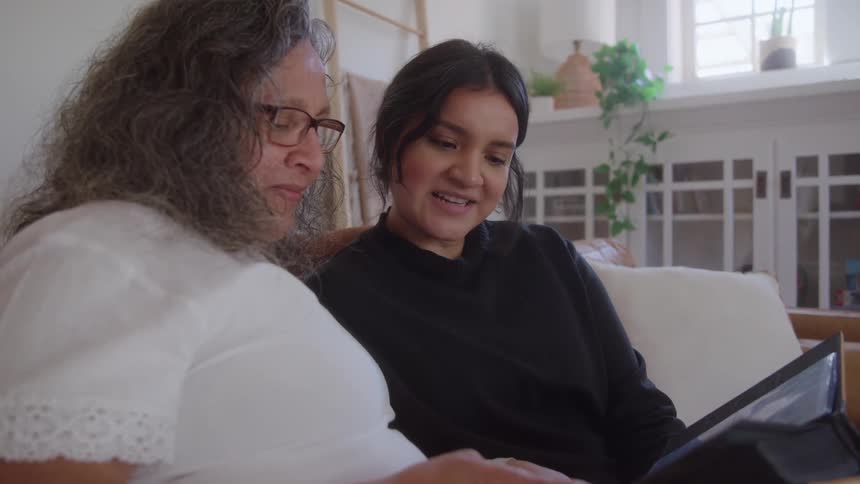 Two people sitting on couch flipping through photo album smiling in cozy welllit room