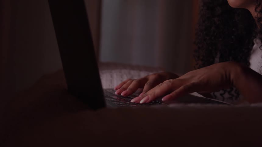 Person lying down types on laptop in dimly lit setting