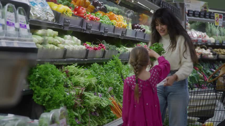 Woman and girl interact while selecting fresh produce in grocery store