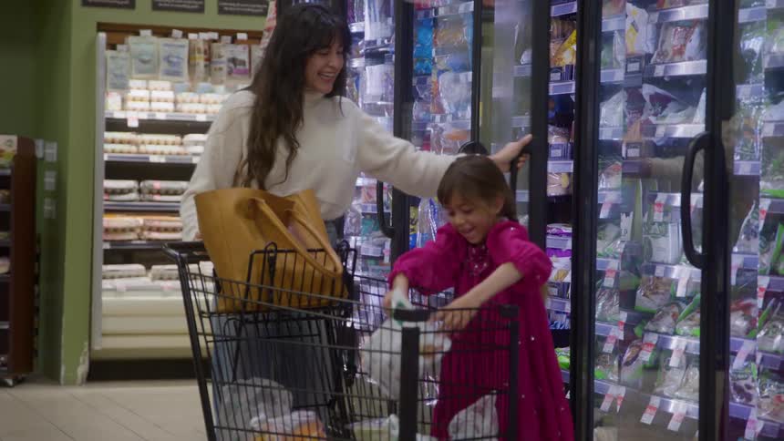 Woman pushes cart as child lifts package in frozen food section