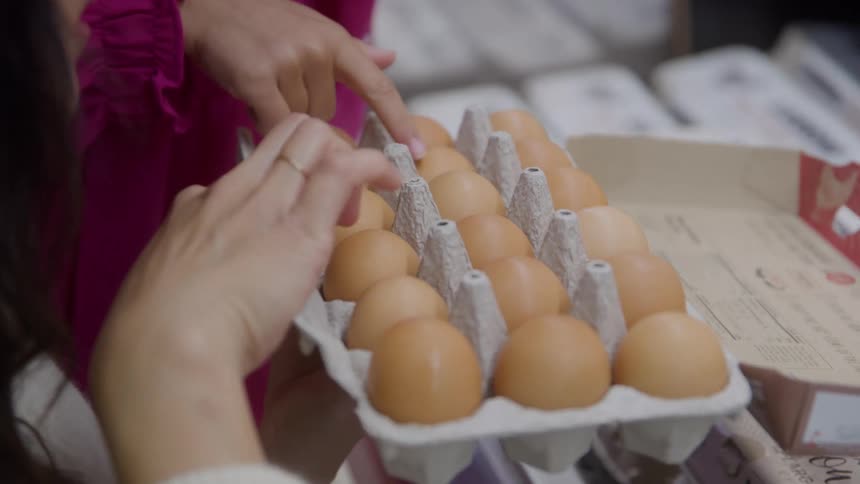 A woman opens a crate of eggs inside a retail shop inspecting their quality by gently touching them