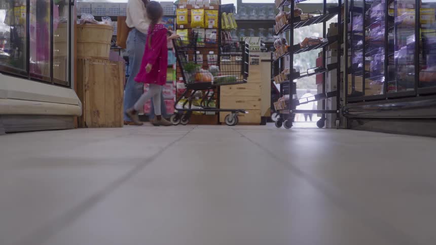 Adult and child walk together pushing cart down grocery aisle