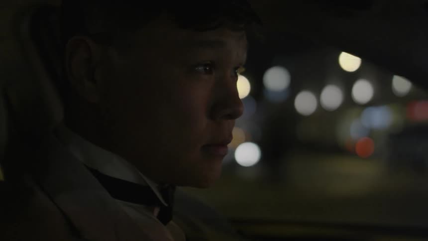 Man wearing a bow tie sitting in his car in a city waiting for the traffic to go by