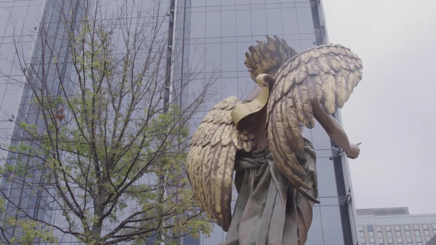 Golden statue of winged figure before modern building blends classical art with contemporary architecture