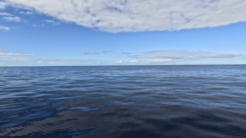 Blue sea surface reflects the partly cloudy sky