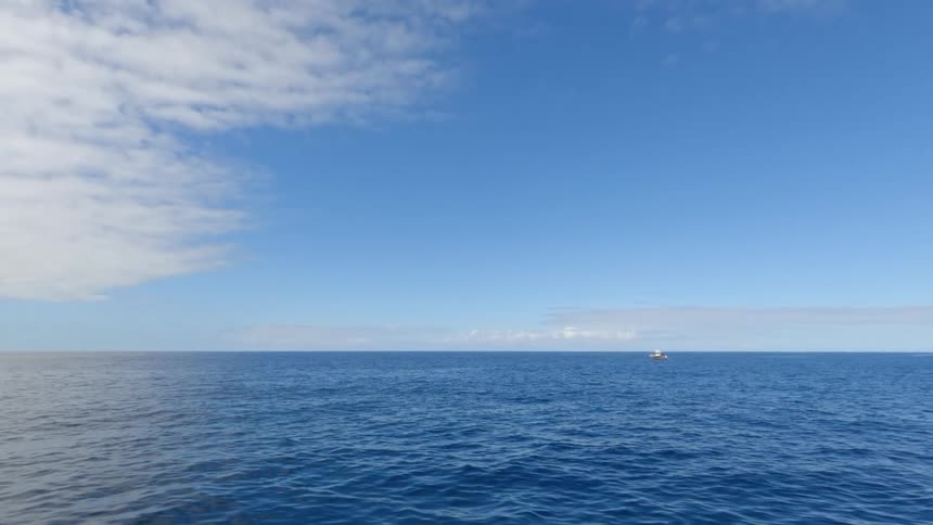 Blue horizon stretches over calm sea with a small boat in the distance