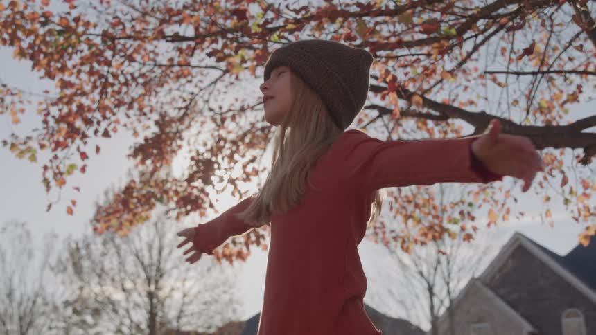 Girl with outstretched arms enjoys autumn weather beneath colorfulleaved tree