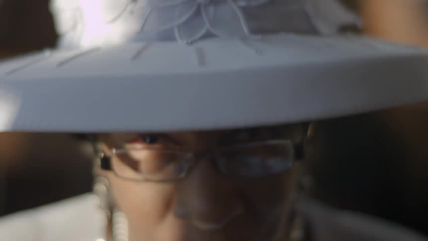 Older woman adjusting her glasses and fancy white hat