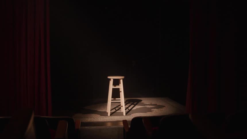 Wooden stool under spotlight on stage framed by red curtains