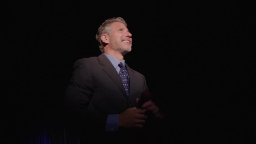 Smiling speaker raises his arm in a farewell gesture on stage