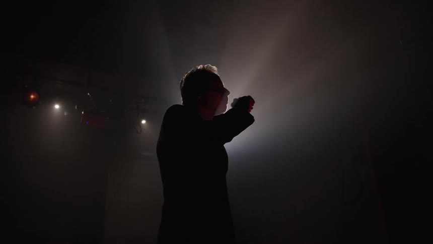 The silhouette of a man speaking in a completely dark environment with a large bright spotlight behind him