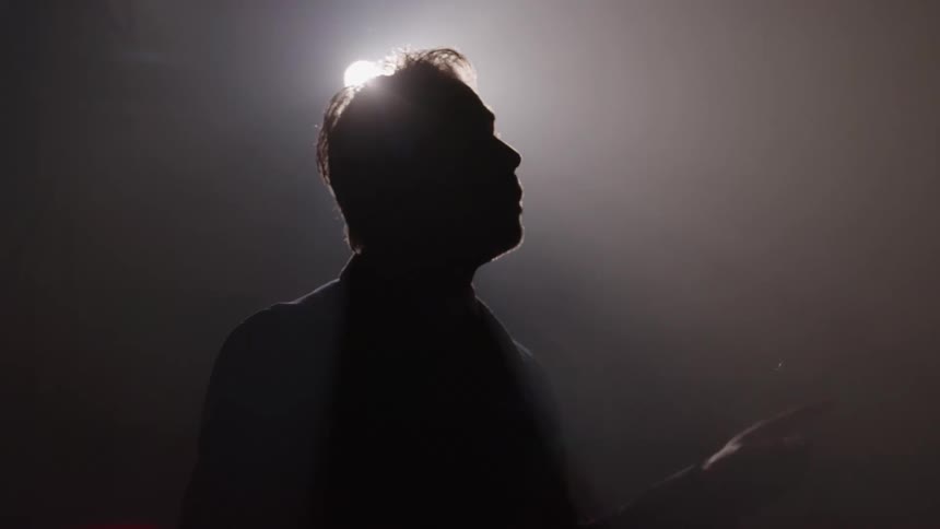 Silhouette of person speaking with raised hand under bright light