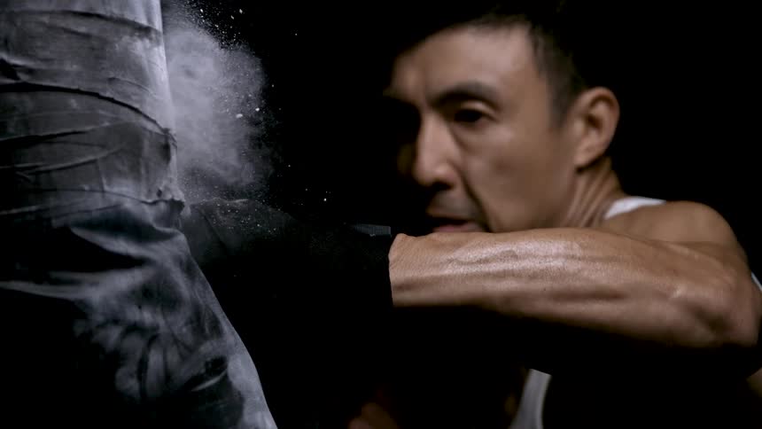 With intense focus a martial artist practices a powerful punch on a training post in slow motion sending dust flying