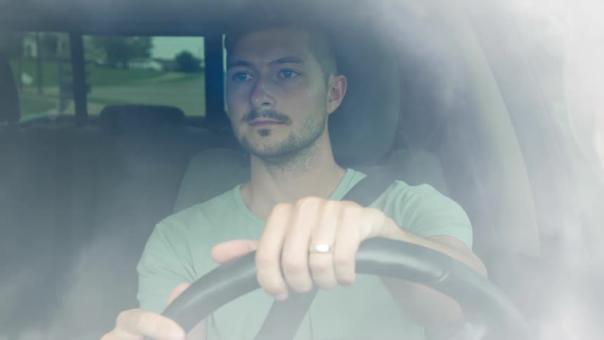Seen through the windshield a young man with a focused expression drives a car