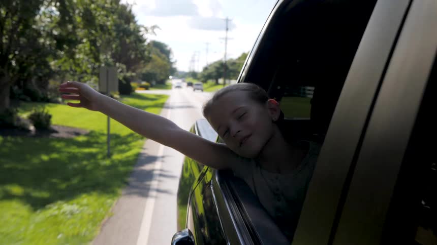Smiling child stretches an arm out of a car window while riding