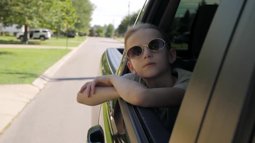 Boy wearing sunglasses leans out of the open truck window as they travel through the neighborhood