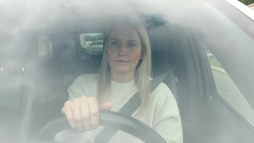 Woman drives with a focused expression as seen through a fogged windshield