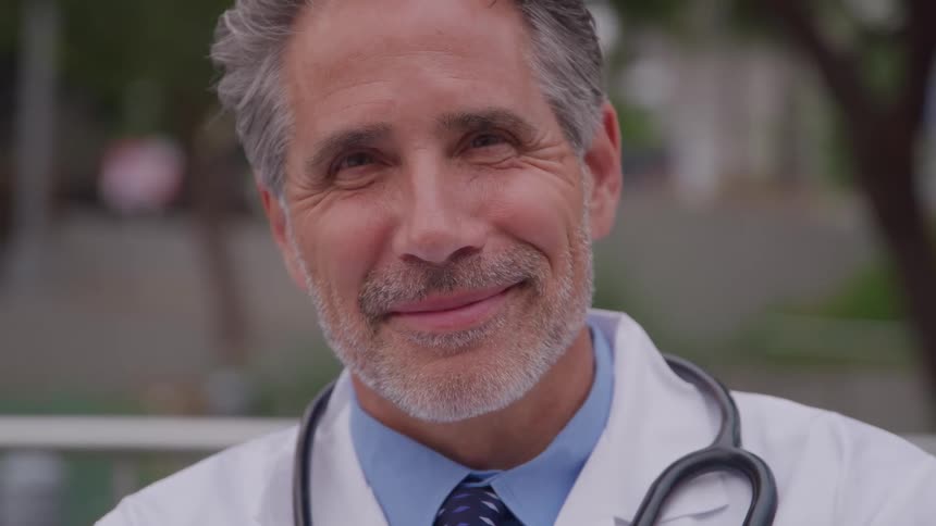 Smiling doctor in a lab coat with a stethoscope outdoors