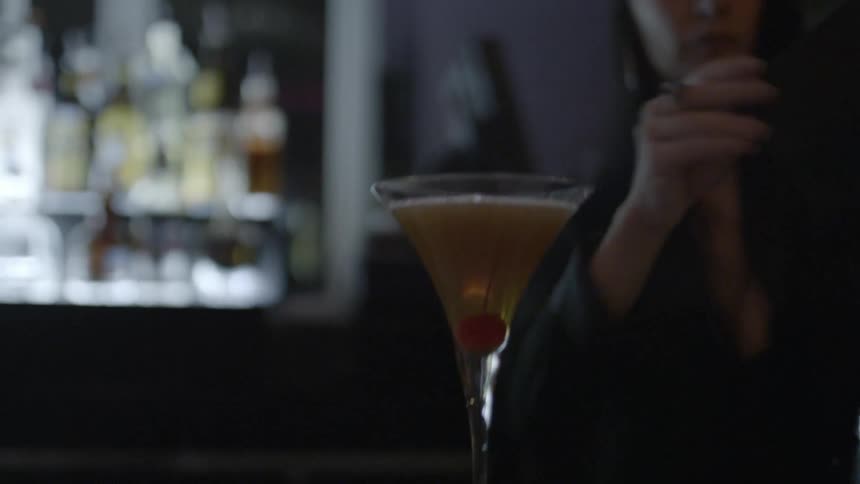 Bartender making a drink and then putting a cherry in it before serving it to her customer