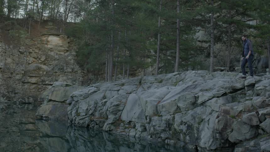 Man stands at the edge of a rocky cliff overlooking a lake