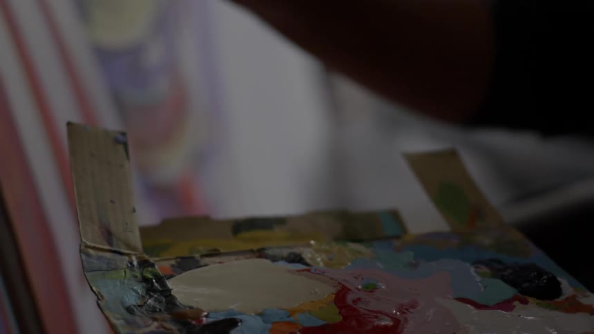 A painter holding a pallet and painting on a canvas