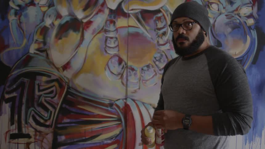 Bearded man removing the cap off a red bottle before a wall that has graffiti-like painting on it