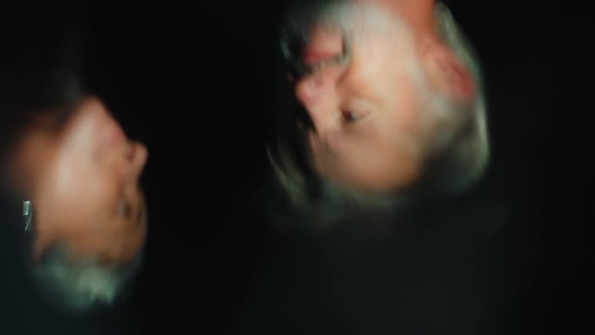 A middleaged man and woman with grey hair are reflected in a puddle of water their figures visible as they stare at each other in a dark room