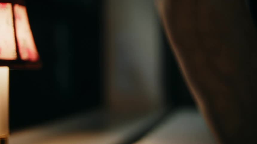 Sheer light brown curtain waving over a window sill next to a lamp indoors during night time