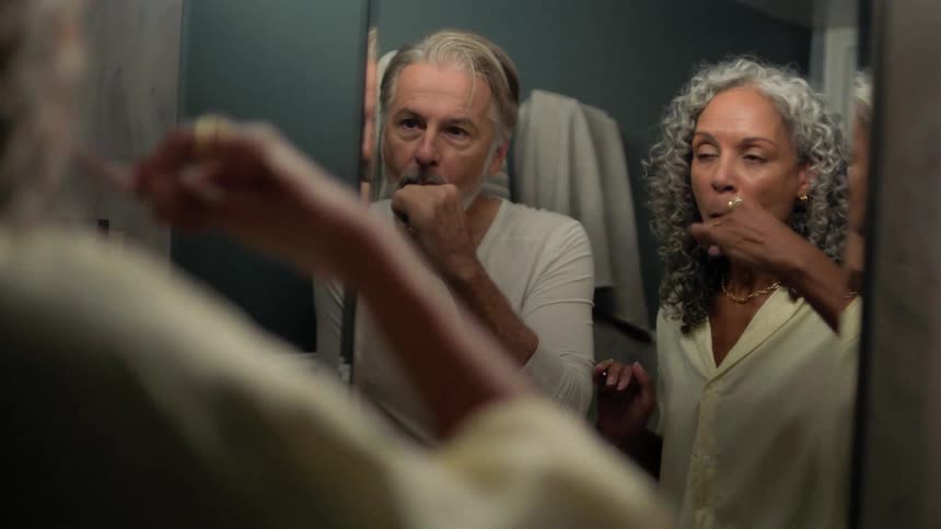 Couple brushes their teeth in front of the mirror while chatting animatedly