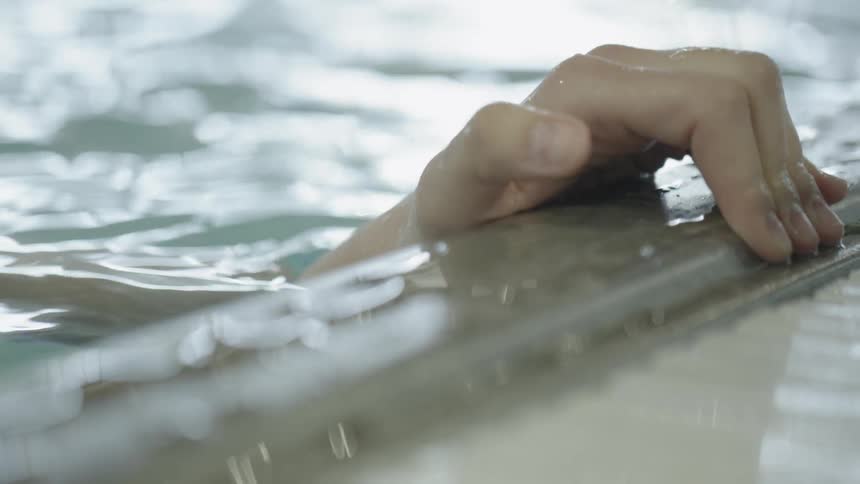 A person grabs the lip of a pool from the water