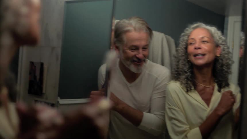 A woman smiles and sings while brushing her teeth with her male companion