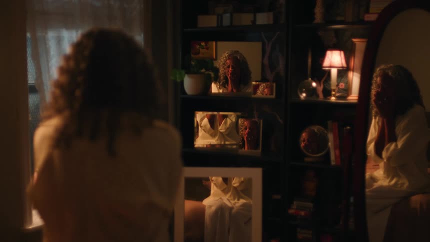 A female is sitting on a bed across from a mirrored bookcase crying