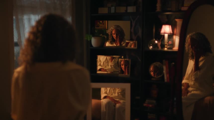 Woman appears reflected in multiple mirrors while sitting in a warmly lit room